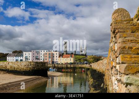 Blick auf den Hafen vom Pier in St. Andrews mit farbenfrohen Gebäuden am Wasser, kleinen Booten im Gezeitenkanal, reflektierendem Wasser und dem dramatischen Ru Stockfoto