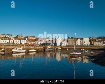 Bei Ebbe liegen farbenfrohe kleine Boote im Hafen von St Monans, deren Reflexionen sich im ruhigen Wasser neben Reihen traditioneller Küstenhäuser und spiegeln Stockfoto