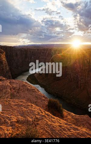 Sonnenuntergang über der tiefen Sandsteinschlucht mit sich windendem Fluss, von der felsigen Klippe unter teilweise bewölktem Himmel aus gesehen Stockfoto