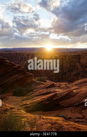 Sonnenuntergang über einer tiefen Schluchtlandschaft mit geschichteten Felsformationen und dramatischen Wolken in einer trockenen Wüstenumgebung Stockfoto