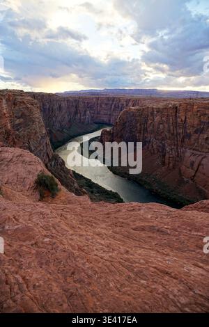 Der sich windende Fluss fließt durch eine tiefe Sandsteinschlucht mit steilen Felswänden unter bewölktem Himmel, von der erhöhten Klippenkante aus gesehen Stockfoto