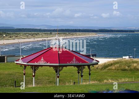 St. Andrews-Bandstand mit kunstvollem rotem Dach auf grasbewachsenen Dünen mit Blick auf den Sandstrand und die abgehackte Nordsee, mit Spaziergänger am Ufer und einer Szenerie Stockfoto