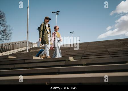 Vielfältige Touristen, die mit Gepäck die Stufen der Stadt hinunterlaufen, lächeln und einen sonnigen Tag genießen Stockfoto
