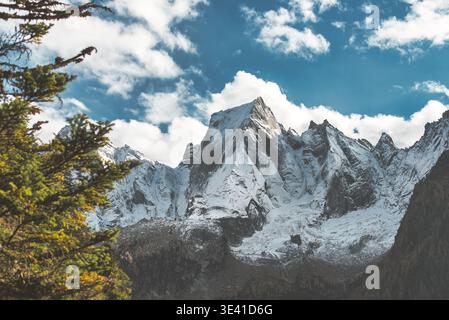 Dramatische alpine Landschaft mit schneebedeckten Berggipfeln, umrahmt von immergrünen Bäumen, unter einem hellblauen Himmel mit verstreuten Wolken Stockfoto