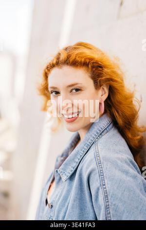 Junge Frau mit rotem Haar, die selbstbewusst lächelt und in die Kamera blickt Stockfoto
