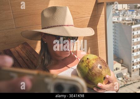 Frau, die sich auf einem Balkon entspannt, frisches Kokoswasser trinkt, Urlaub genießt Stockfoto