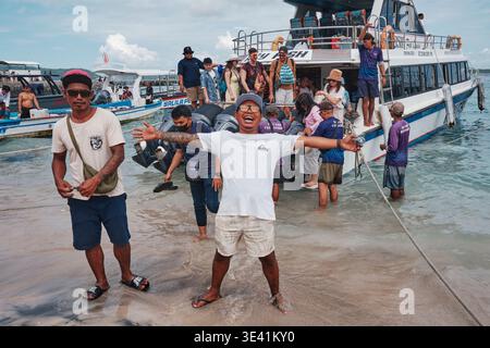 Ein ortskundiger Reiseleiter begrüßt die Besucher mit offenen Armen und einem Lächeln. Die Menschen versammeln sich am Ufer, als ein Boot in Nusa Penida ankommt. Einige kommen davon, was sie tun Stockfoto