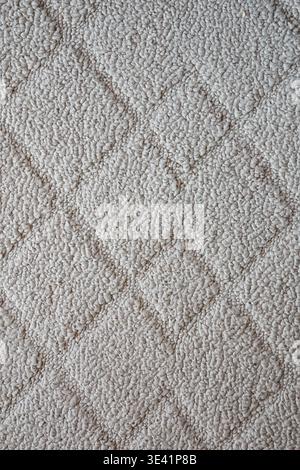 Nahaufnahme eines weichen beigefarbenen Teppichs mit rautenförmigen, erhöhten und vertieften Texturen, die das geometrische Textildesign hervorheben. Stockfoto