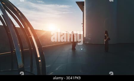 Mann fotografiert Frau bei Sonnenuntergang im modernen urbanen Raum mit warmem Licht, Paare, die während der goldenen Stunde Erinnerungen mit Silhouette und Kinofilm schaffen Stockfoto