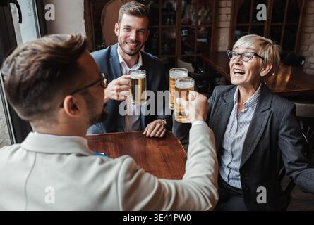 Eine Geschäftsfrau sitzt mit ihren jüngeren männlichen Kollegen im Café, bremst und trinkt Bier. Stockfoto