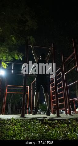 Ein Mann, der nachts an den Bars im Freien trainieren kann, ein männlicher Athlet, der im Park Calisthenics-Workout durchführt Stockfoto
