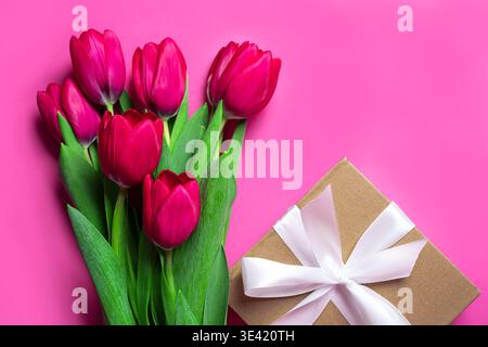 Tulpen und Geschenkbox mit Band auf lila rosa Hintergrund, Draufsicht, Kopierraum. Muttertag-Designvorlage, Weihnachtskonzept mit Tulpen. Stockfoto
