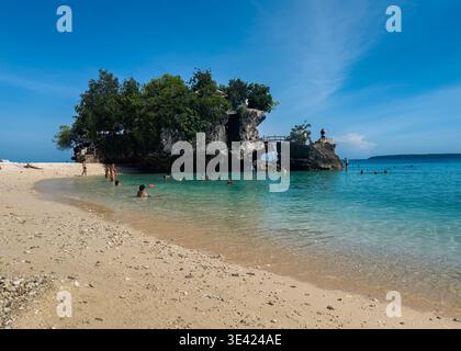 Besucher schwimmen und entspannen am Salagdoong Beach, Siquijor, Philippinen, mit klarem türkisfarbenem Wasser, weißem Sand und üppiger tropischer Umgebung. Stockfoto