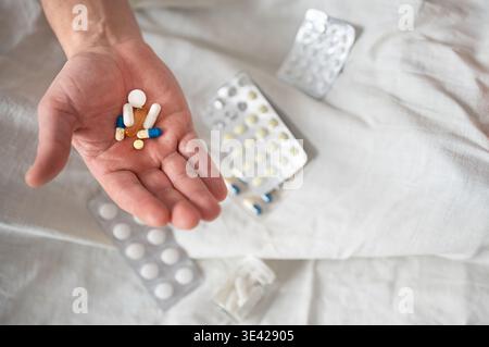 Haufen von verschiedenen bunten Pillen und Kapseln in der Hand auf weißem Blatt Hintergrund mit anderen Blisterpackungen von Arzneimitteln. Senior Mann, der Medizin oder Sup nimmt Stockfoto