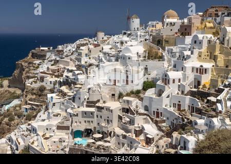 Stadtansicht des Dorfes Oia auf der Insel Santorin mit seinen weiß getünchten Höhlen und Klippenhäusern, Hotels, berühmten Windmühlen und einer kleinen Kirche Stockfoto