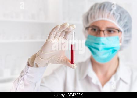 Wissenschaftler halten Blutprobe im Reagenzglas, medizinische Forschung und Labortestkonzept mit Arzt in Schutzausrüstung Hintergrund Stockfoto