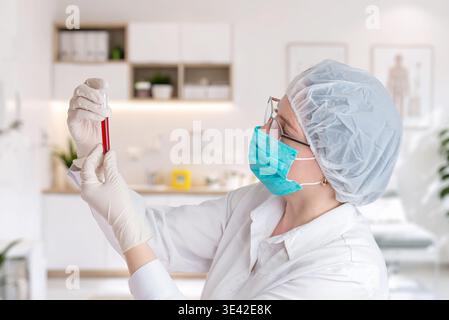 Wissenschaftler untersuchen Blutprobe sorgfältig im Reagenzglas, Gesundheitsforschung und Labordiagnostik-Konzept mit moderner klinischer Innenausstattung Stockfoto