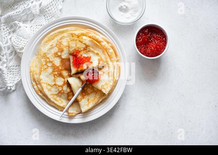 Hausgemachte dünne Crepes mit rotem Kaviar und Creme auf weißem Hintergrund, Draufsicht, Kopierraum. Herzhafte Pfannkuchen mit Lachsfischkaviar. Maslenitsa Pfannkuchen Stockfoto