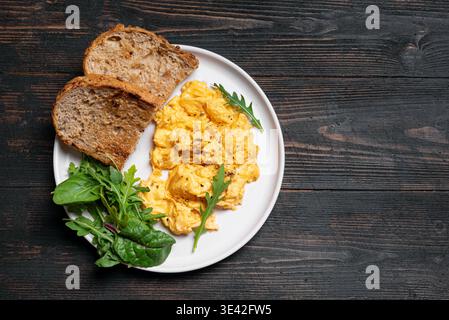 Rührei mit Gemüse für ein gesundes Keto-Frühstück. Teller mit Rührei mit Salatmischung auf rustikalem Holzhintergrund, Blick von oben. Stockfoto