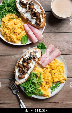 Gesunde, ausgewogene Frühstücksteller. Rührei, Gemüse, Schinken, Sandwich mit Frischkäse und gebratenen Pilzen. Frühstück für zwei, gemeinsames Frühstück Stockfoto