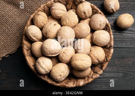 Ganze Walnüsse im runden Korb auf hölzernem Hintergrund, Draufsicht. Korb mit Walnüssen. Paleo-Diät und gesundes Esskonzept. Stockfoto