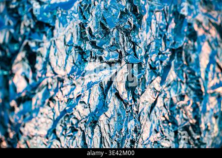 Zerknitterte Aluminiumfolie schafft eine abstrakte blaue Textur mit metallischen Reflexen und Schatten Stockfoto