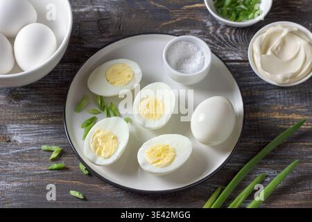 Gekochte Eier mit grüner Zwiebel, Salz und Mayonnaise auf Teller auf Holztisch Stockfoto