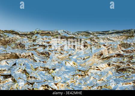 Zerknitterte Aluminiumfolie schafft eine abstrakte silberne Metallic-Landschaft unter blauem Himmel Stockfoto