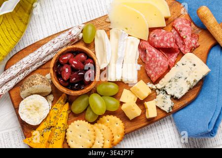 Antipasti auf einem Holzbrett mit verschiedenen Käsesorten, Wurstwaren, Oliven und Trauben Stockfoto