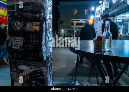 Altes öffentliches Telefon mit Aufklebern neben einem Stehtisch mit Getränken in der Nähe des Eingangs zum RAW-Gelände in Berlin Friedrichshain. Stockfoto