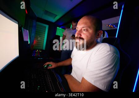 Fokussierter Gamer Mann, der mit Freunden hinter dem PC im neonbeleuchteten Gaming Room spielt Stockfoto