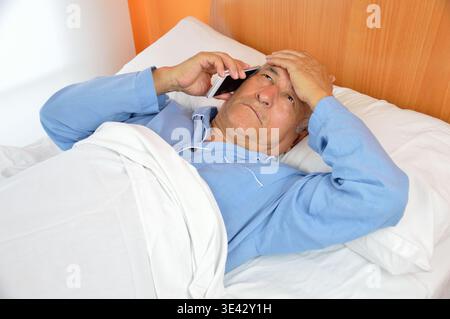 Kranker Seniorenmann im Bett und rief den Arzt mit Telefon an Stockfoto