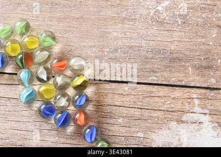 Transparenter Glasmarmor auf einem rustikalen Holztisch mit lebhaftem farbenfrohen Hintergrund. Künstlerische Komposition mit Reflexionen, Texturen Stockfoto
