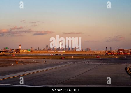 Start- und Landebahn am Newark Liberty International Airport während der goldenen Stunde mit der Skyline von Manhattan im Hintergrund. Sonnenlicht reflektiert von Wolkenkratzern Stockfoto