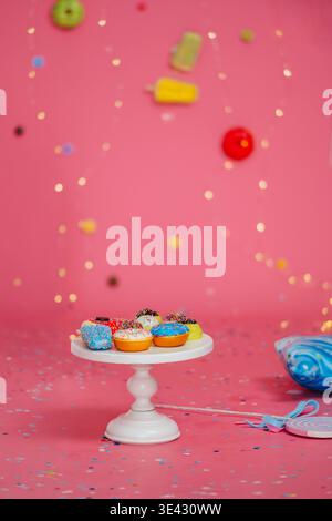 Bunte Donuts Auf Weißem Sockel, Leuchtendes Rosafarbenes Hintergrund Mit Süßigkeiten Und Konfetti Stockfoto