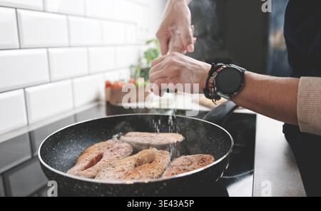 Girl Salts Red Fish Lachs, der in Einer Pfanne auf dem Küchenherd gebraten wird Stockfoto