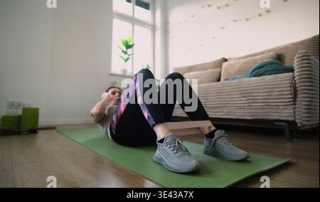 Mädchen macht Fitnessübungen mit Gummiband, macht Abs-Übungen auf dem Boden Stockfoto