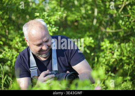 Ein reifer Mann befindet sich inmitten eines üppig grünen Waldes, erkundet die Natur mit seiner DSLR-Kamera und macht Fotos Stockfoto