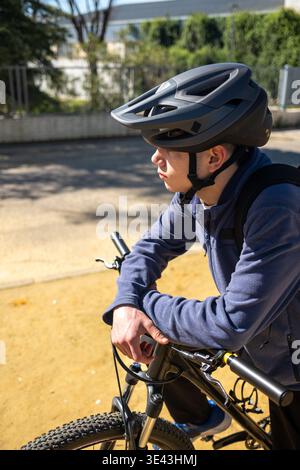Junger Radfahrer, der einen Schutzhelm und Rucksack trägt und im Freien die Arme auf seinem Mountainbike überkreuzt hat Stockfoto