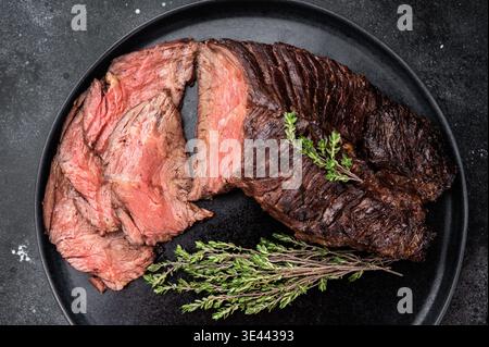 Geschnittenes gegrilltes Rindersteak oder Onlet Steak auf schwarzem Teller mit Thymian und Salz, dunkler Steinhintergrund mit Kopierraum Stockfoto