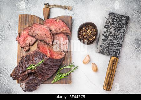 Gekochtes Hänger Steak Zwerchfellfleisch geschnitten mit saftigem mittlerem Garn, Kräutern Knoblauch und Gewürzen an Bord, sauberer heller Hintergrund Stockfoto