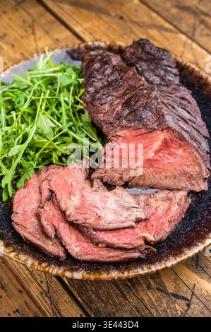 Closeup gegrilltes onglet Hängersteak mit Rucola-Salat auf Servierteller, gebratener Kruste und zartem Interieur auf rustikalem Holzhintergrund Stockfoto