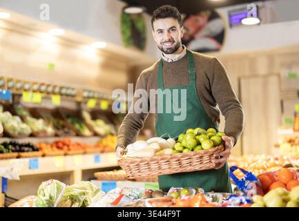 Mann Angestellte in Uniform tragen Korb mit verschiedenen Gemüse und Früchten im Lebensmittelgeschäft Stockfoto