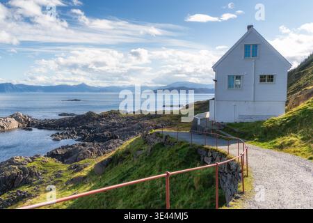 Regionaler Kontext für den Leuchtturm an der norwegischen Atlantikküste. Der geschwungene Weg führt zu einem weißen Gebäude auf felsigem Hang, das die lokale Geschichte und Geschichte widerspiegelt Stockfoto