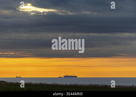 Ein atemberaubender Sonnenuntergang blickt auf Schiffe am fernen Ozeanhorizont inmitten eines dramatischen Wolkenhimmels Stockfoto