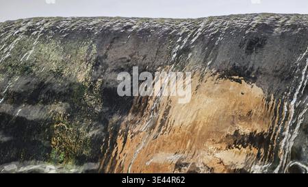 Abstrakte Textur von Wasser, das über einen moosigen und felsigen Rand kaskadiert. Stockfoto