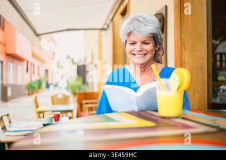 Seniorin liest Bücher während des Frühstücks vor der Kaffeebar - Freizeitaktivitäten und Relax Life Konzept Stockfoto