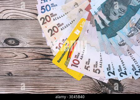 KIEW, UKRAINE - 28. JANUAR 2026 Bankolombienkarte und kolumbianische Peso-Geldscheine auf dem Tisch in Nahaufnahme. Bancolombia ist die beliebteste Bank in Kolumbien Stockfoto
