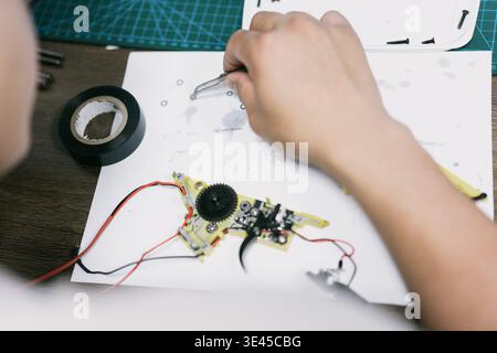 Nahaufnahme der Hände mit einer Pinzette zur Reparatur der elektronischen Leiterplatte mit Zahnrädern und Drähten auf weiß Stockfoto