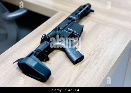 Schwarzes Gewehr im Stil AR-15 auf Holztisch in moderner Inneneinrichtung Stockfoto